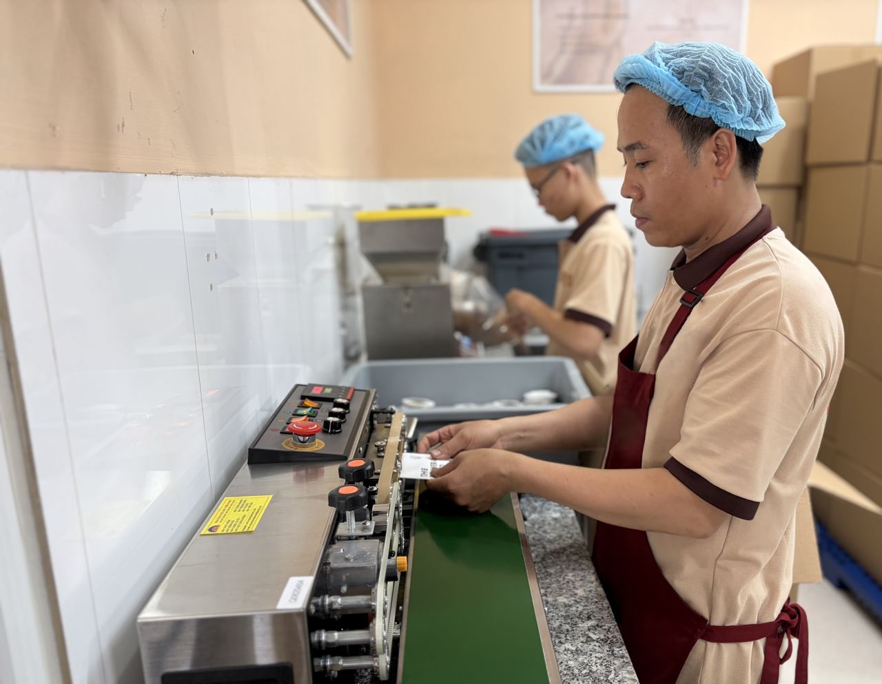 Tung氏の会社のコーヒー包装ラインで、衛生帽を着用した作業員がパッケージング作業を行う様子